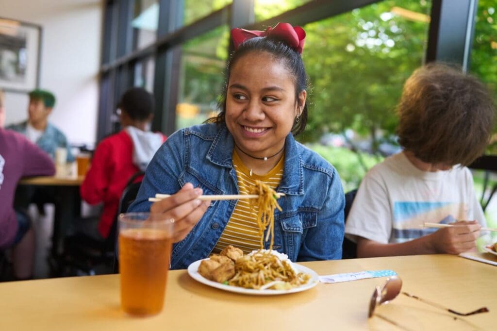 A middle school girl smiles while eating her school lunch.