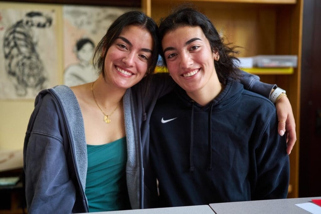 Two high school sisters smile together in the art room.