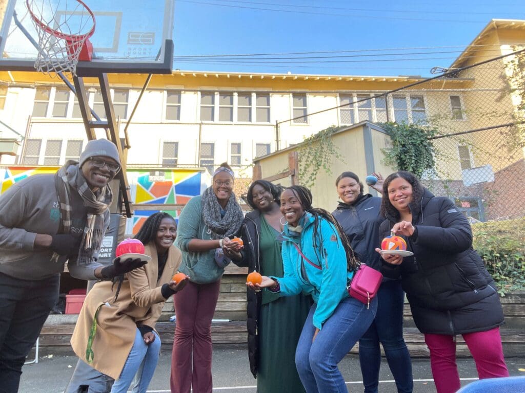 A group of teachers smile for a photo and show off their painted pumpkins.