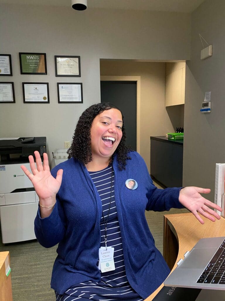 A faculty member smiles at her desk in the front office.