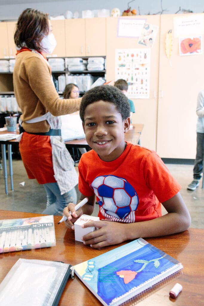 Picture of an elementary student wearing a soccer shirt working on an art project at school.