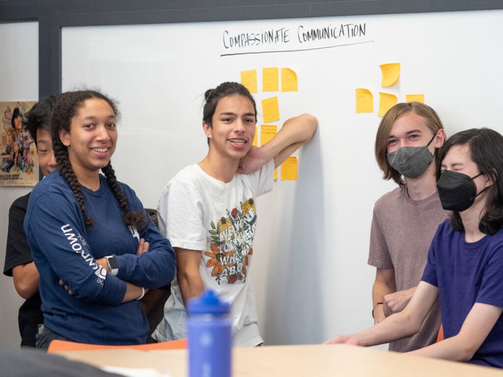 Group of high school students from the Downtown school gathered around a whiteboard.